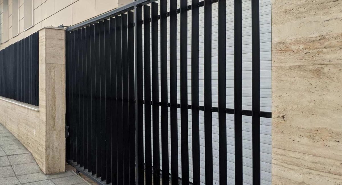 Modern, custom-designed black metal fence installed against a stone wall, showcasing bespoke fencing solutions in Fargo, ND.